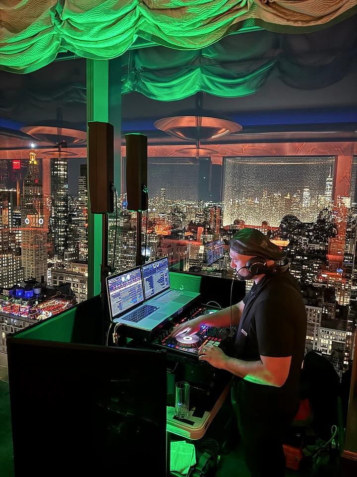 DJ actively mixing at a corporate event with a nighttime city skyline behind the setup.