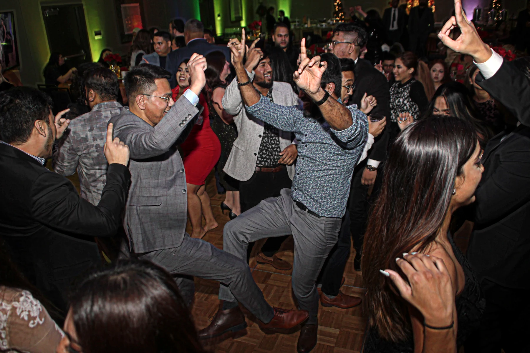 Guests dancing and raising their hands across a crowded dance floor under event lighting.