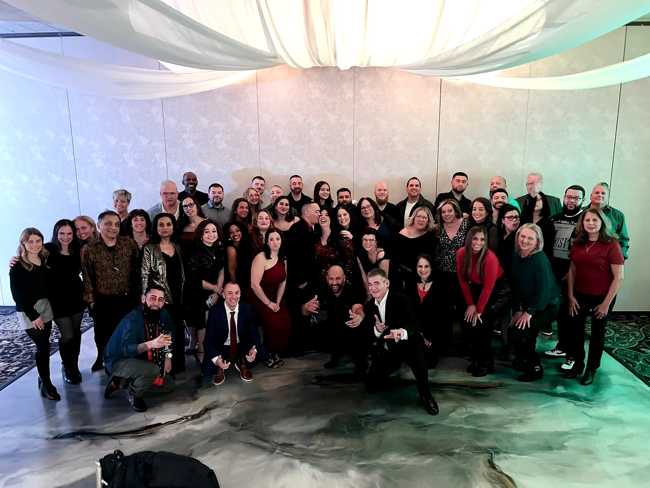 A large team gathered together at a recent company holiday party beneath draped event decor.