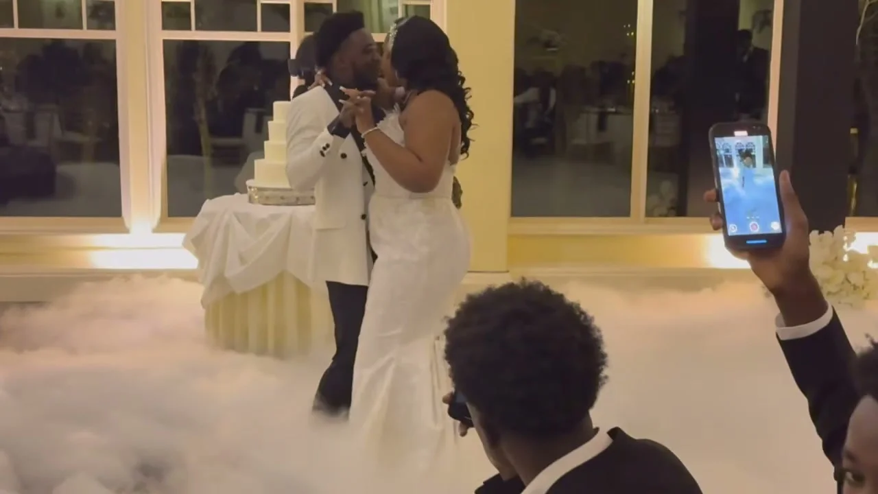 A couple shares a first dance surrounded by a low-lying cloud effect as guests record the moment.